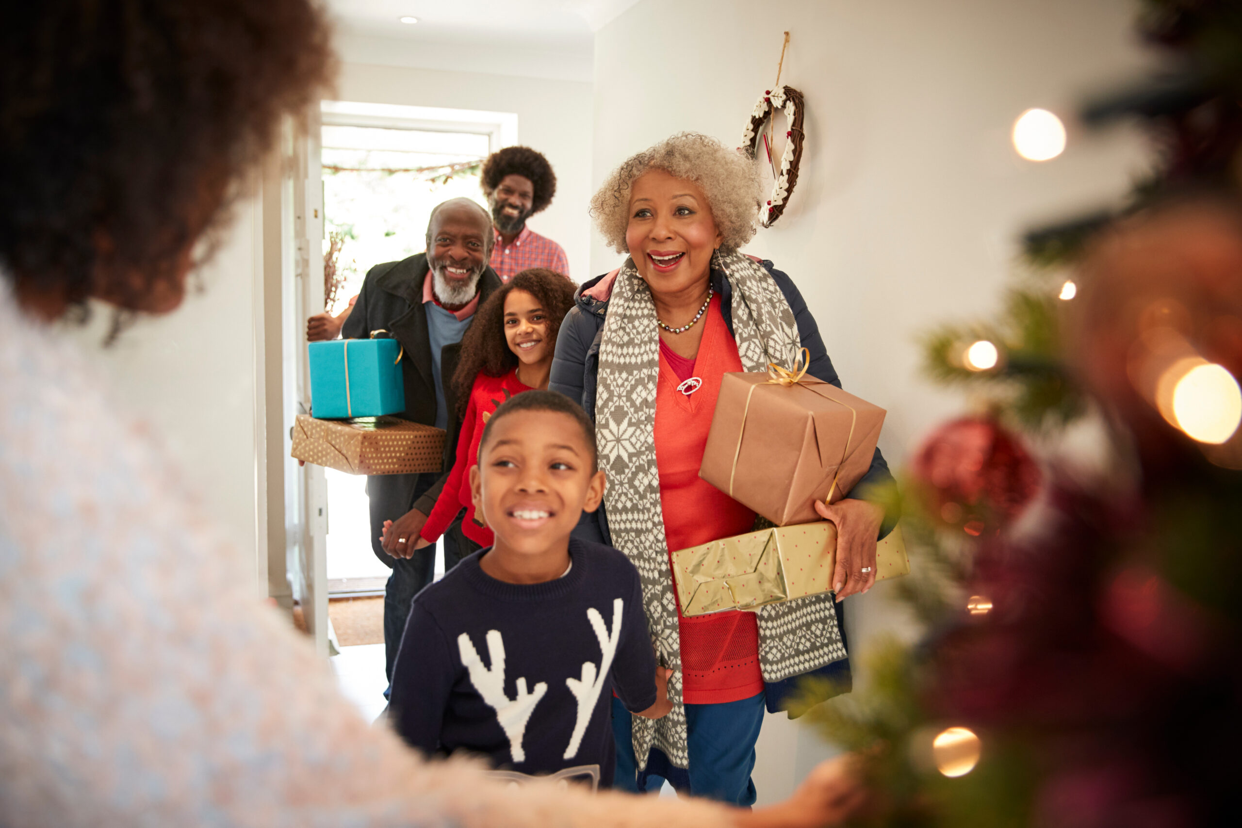 Grandparents Being Greeted By Family As They Arrive For Visit On Christmas Day With Gifts