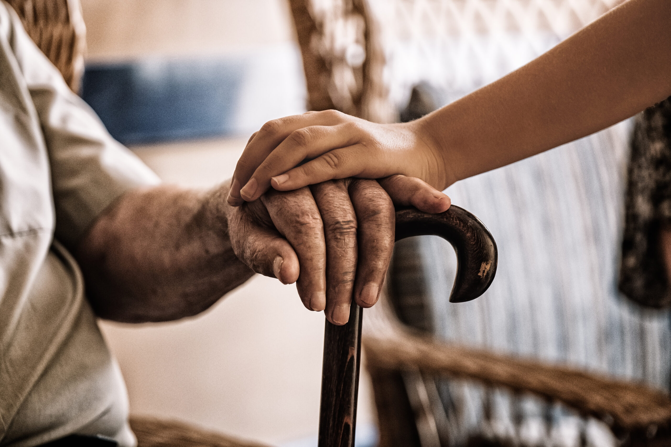 child’s hand over old man’s hand holding a cane.